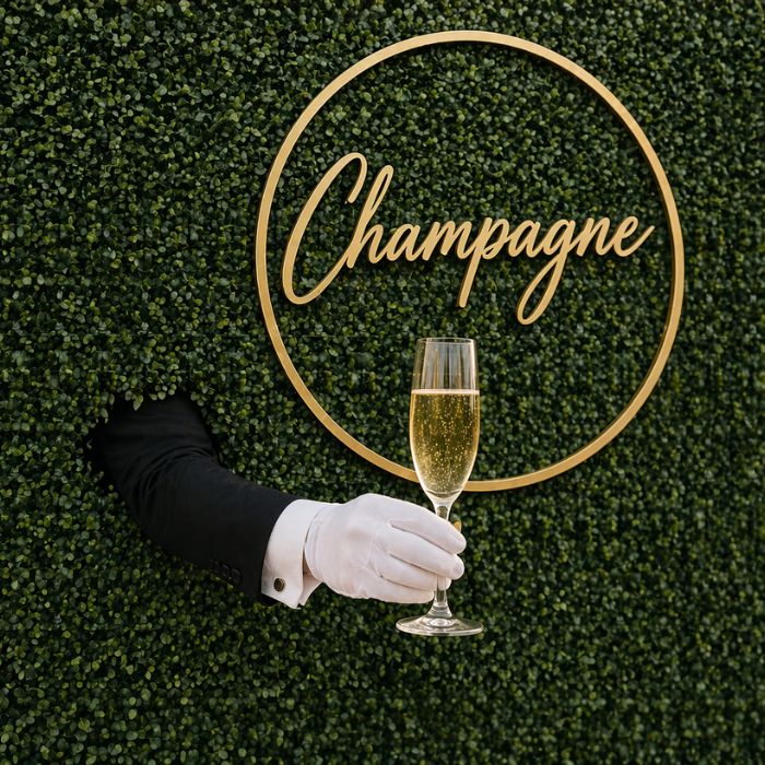 White-gloved hand emerging from hedge with champagne