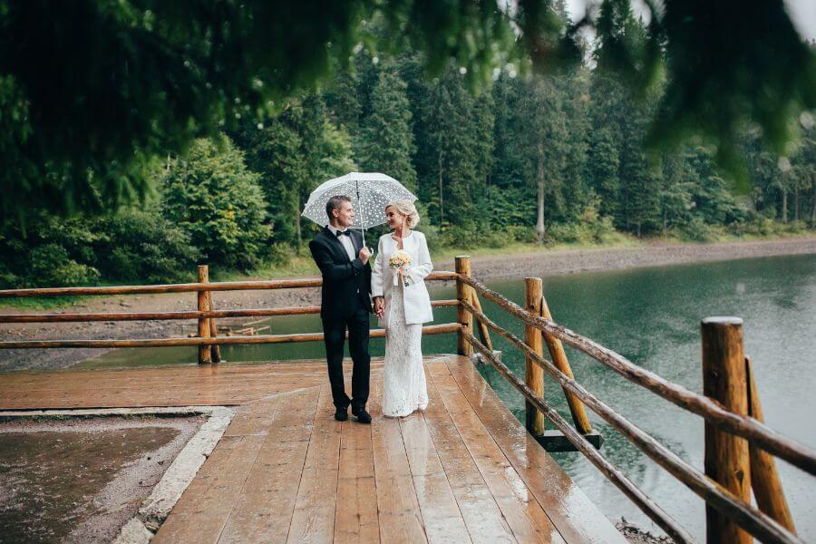 Bride and groom embracing the rain under an umbrella on their wedding day
