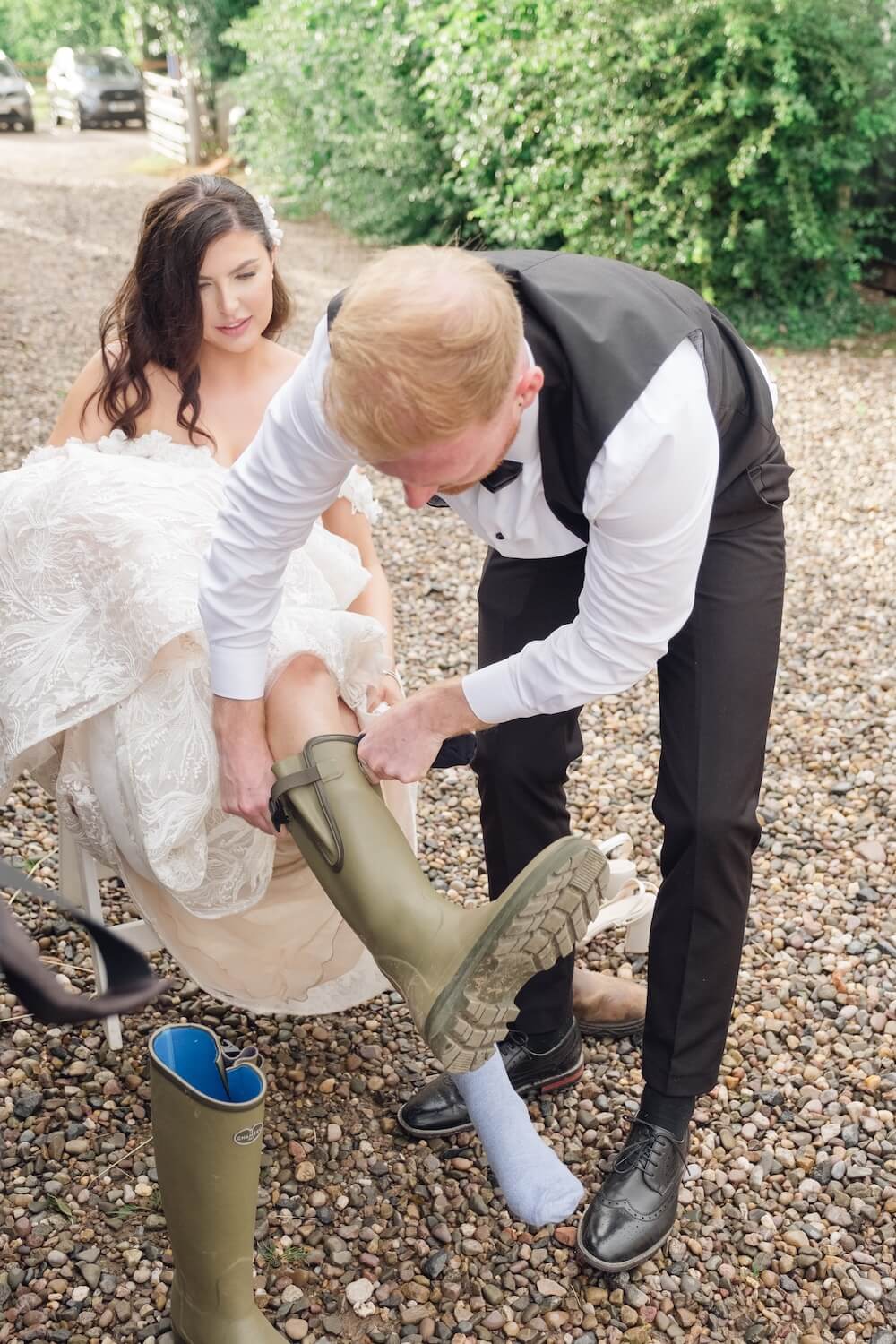 Groom helping bride into her wellies on a rainy wedding day